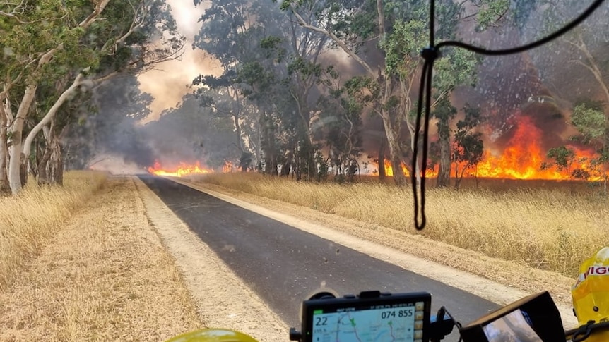 A long line of flames in grass and scrub seen through the windscreen of a fire truck.