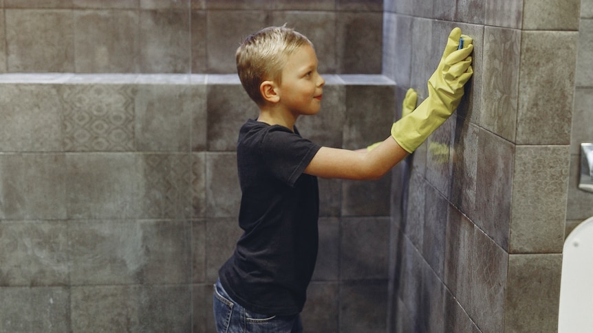 A boy cleans shower walls and time management experts encourages parents to get kids to help around the house