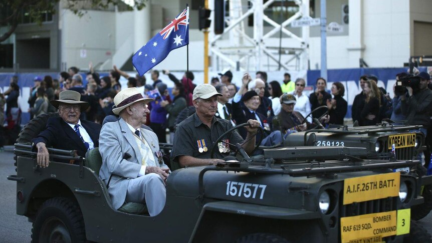 Three veterans sitting in an old army car in an Anzac Day parade.