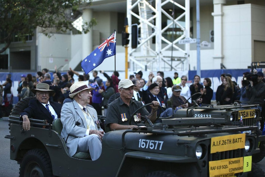 Three veterans sitting in an old army car in an Anzac Day parade.