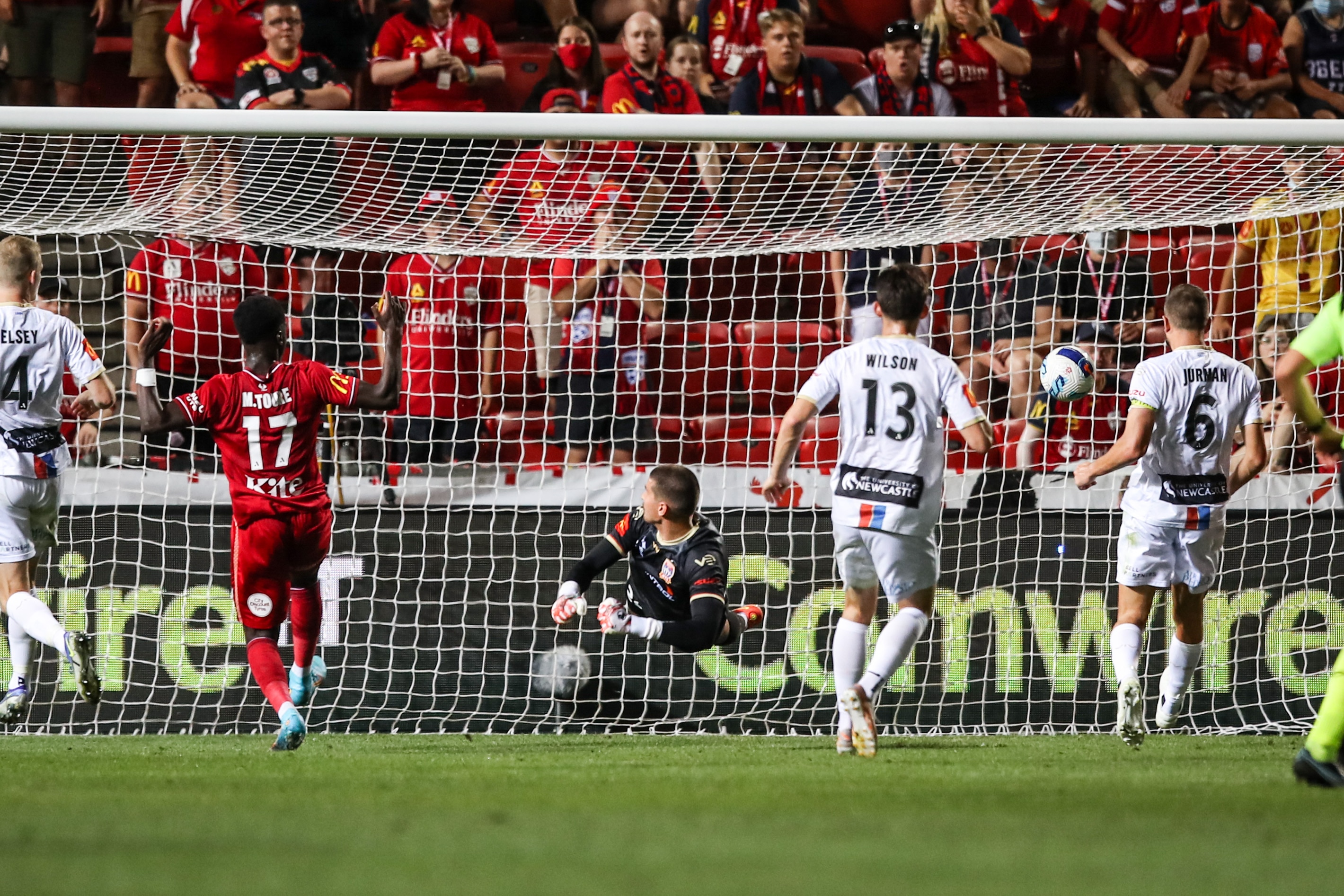 A picture from distance of an Adelaide United A-League player watching his shot go past the goalkeeper into the net.