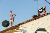 Two people on a tiled roof inspect damage.