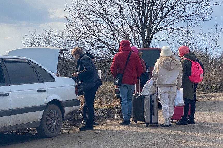 People with suitcases near a car on the road. 