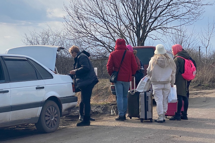 People with suitcases near a car on the road. 