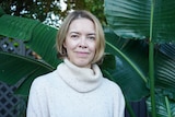 A woman standing in front of large green leaves smiles