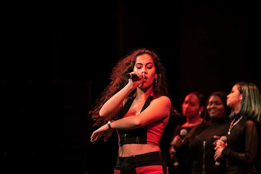 Colour photo of Indigenous Australian-Samoan singer-songwriter Rebecca Hatch singing on stage at Sydney Opera House.