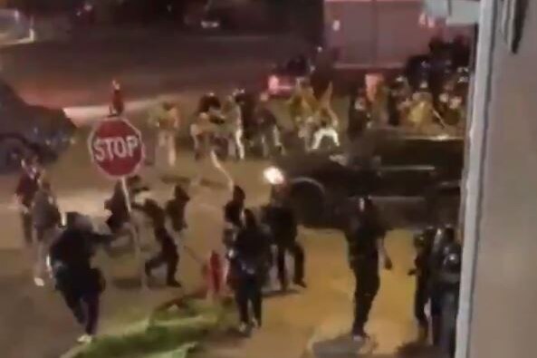 A black SUV is seen driving through a crowd of police at night.