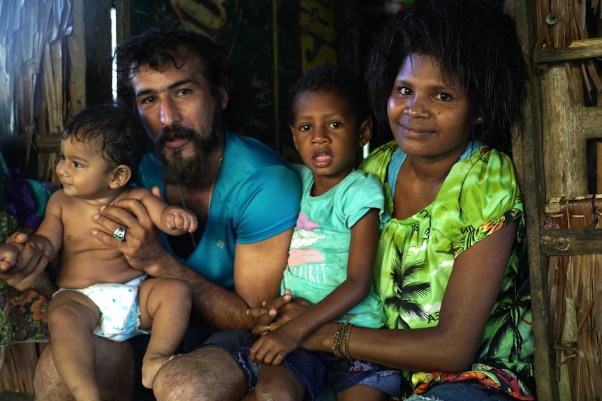 A father holds his baby while sitting next to his wife and stepchild