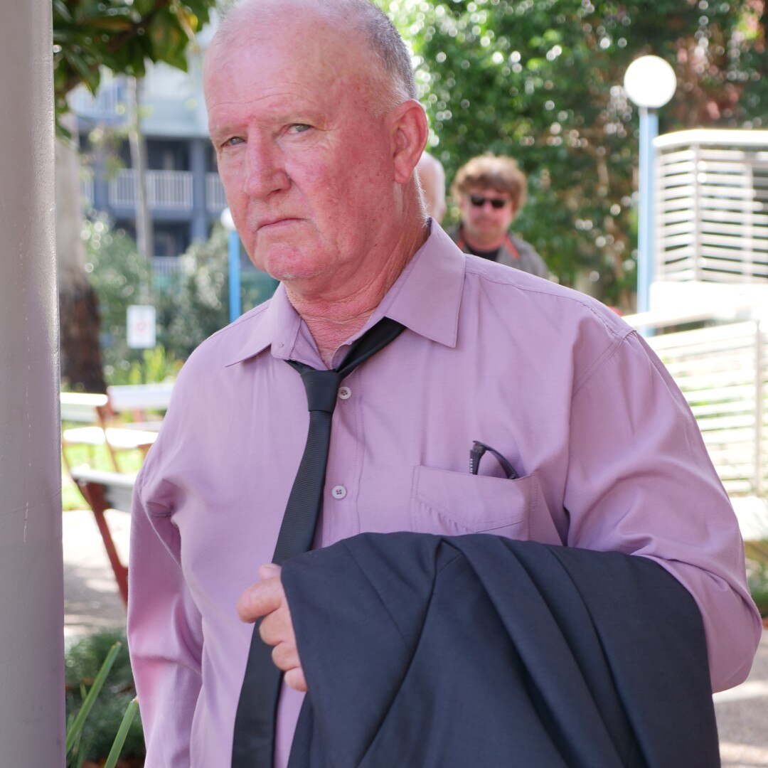 Elderly man in pink shirt stares at camera not smiling 