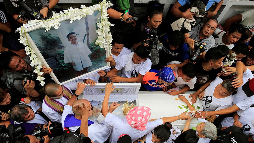 Mourners hold a framed photo of a smiling Kian delos Santos during a crowded funeral in the Philippines.