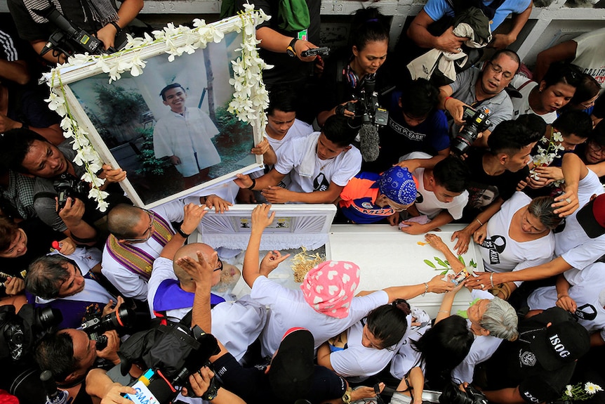 Mourners hold a framed photo of a smiling Kian delos Santos during a crowded funeral in the Philippines.