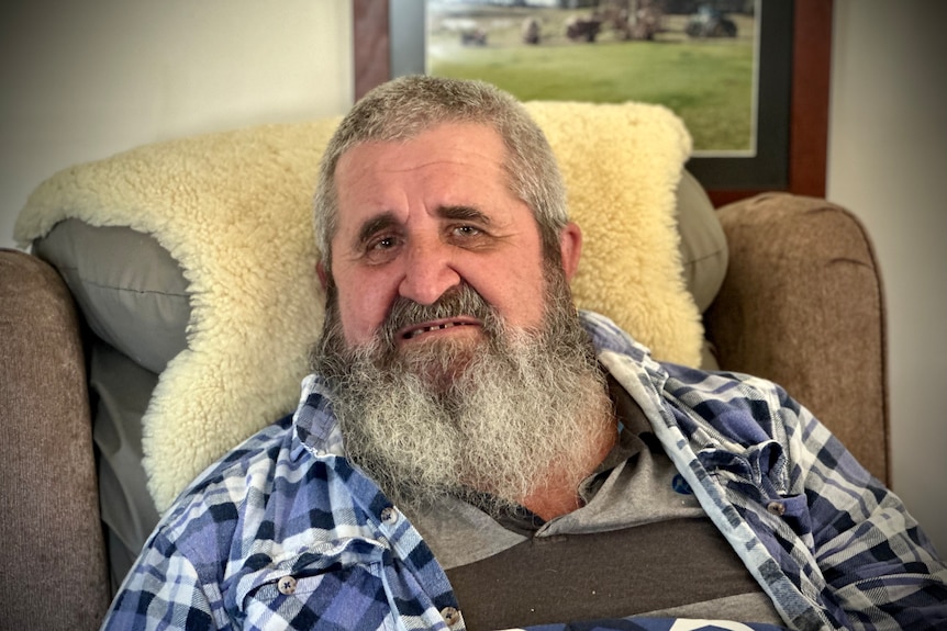 A man with a beard sits on an arm chair