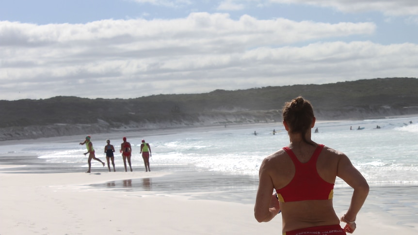 A woman wearing bathers runs along the beach.