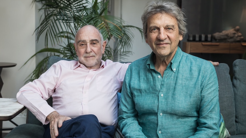 Claude-Michel Schönberg (left) and Alain Boublil (right) sitting on a couch and smiling at the camera.