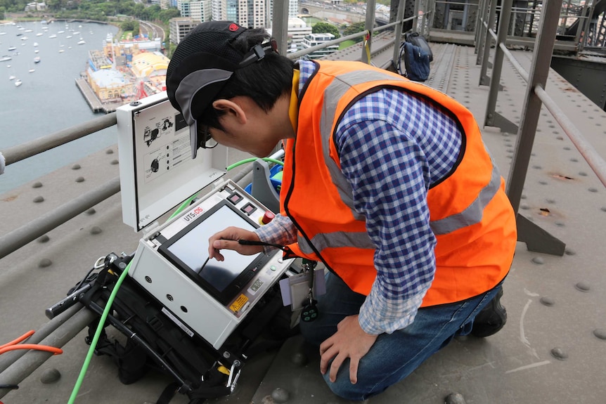 An engineer at work near the summit of the Sydney Harbour bridge inspects the work of a robot used in maintenance works.