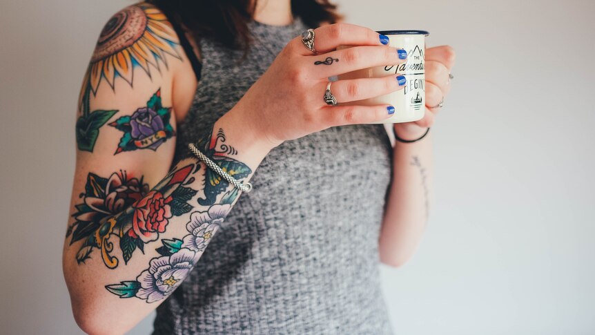 A woman's heavily tattooed right arm, holding a cup of coffee