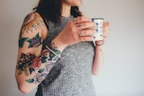 A woman's heavily tattooed right arm, holding a cup of coffee