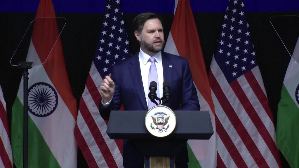 US Vice President JD Vance speaking at a podium, US and Indian flags behind him.
