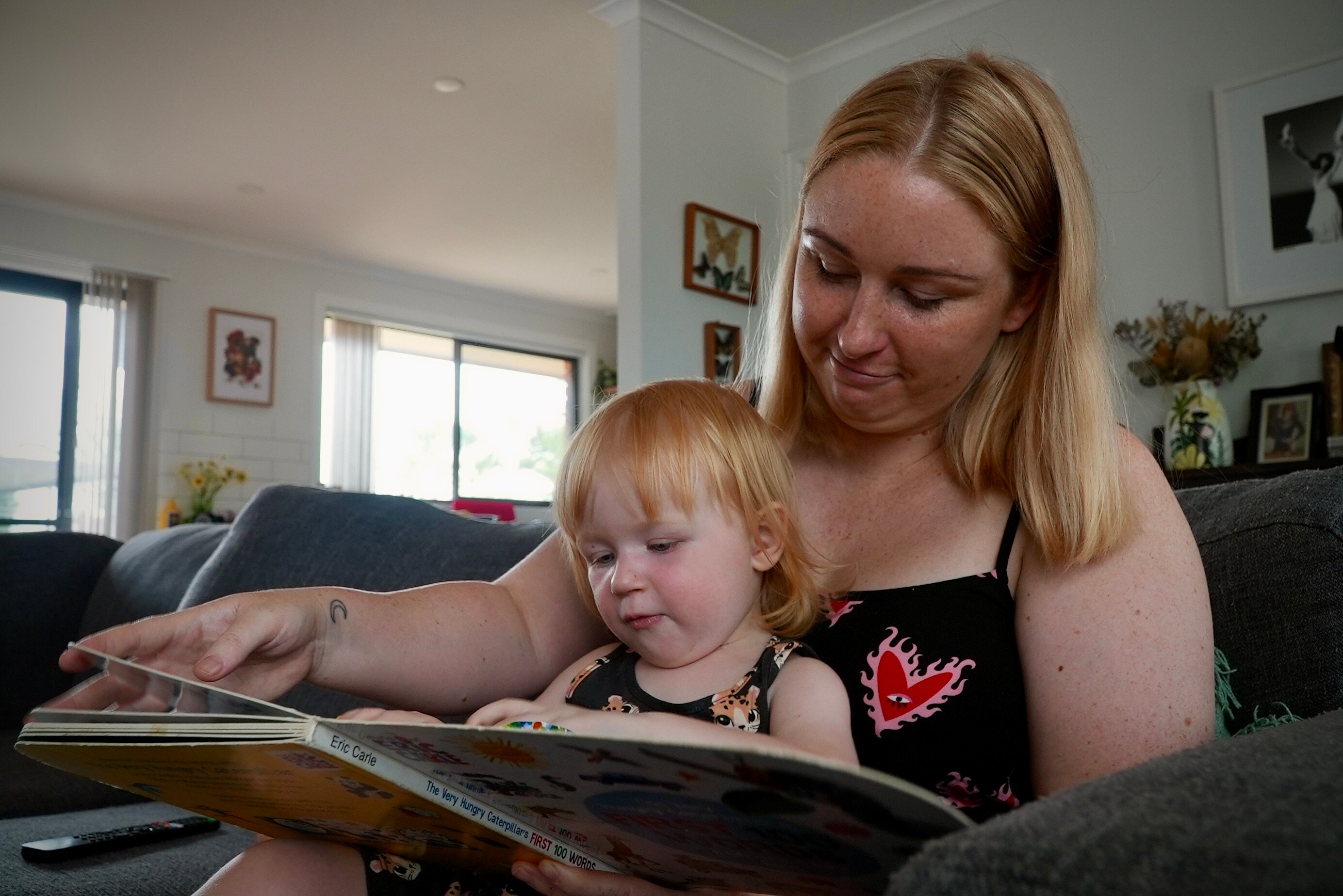 A young white woman with blonde hair sitting on a couch with a baby with red hair