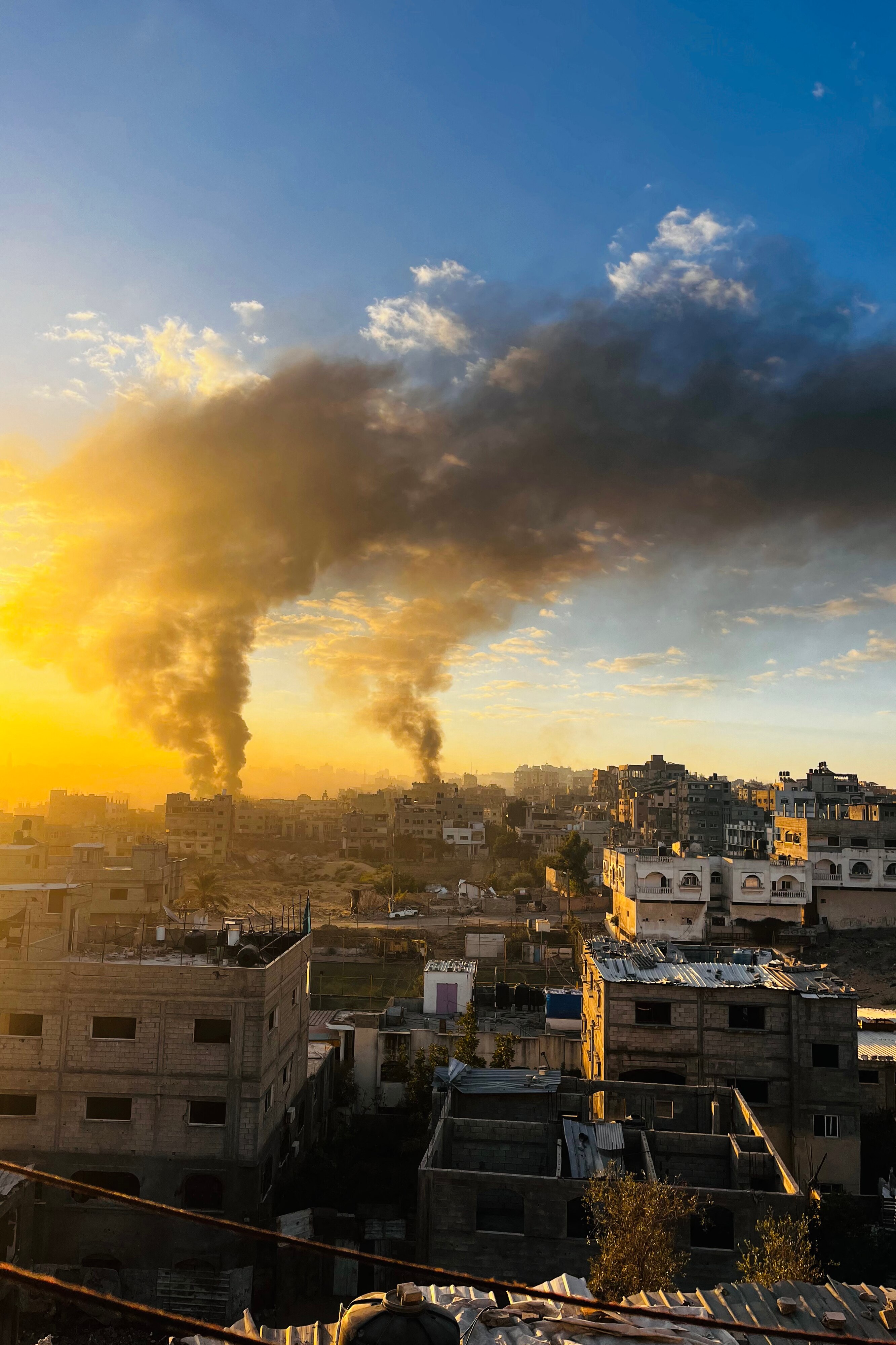 Two plumes of smoke over a city skyline, lit by orange sky.