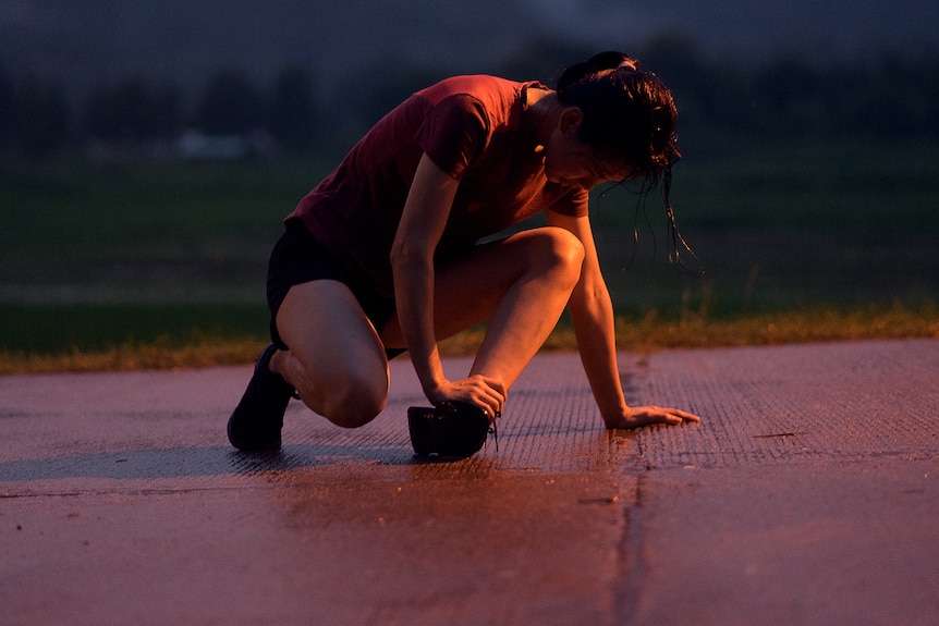 A night-time scene of a runner bent over on the ground clutching their ankle, with head bowed down.