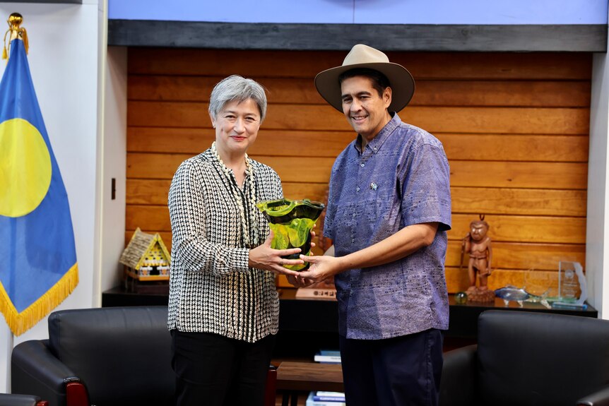 Penny Wong and Surangel Whipps Jr, wearing an Akubra, hold a green vase and smile for photographers 