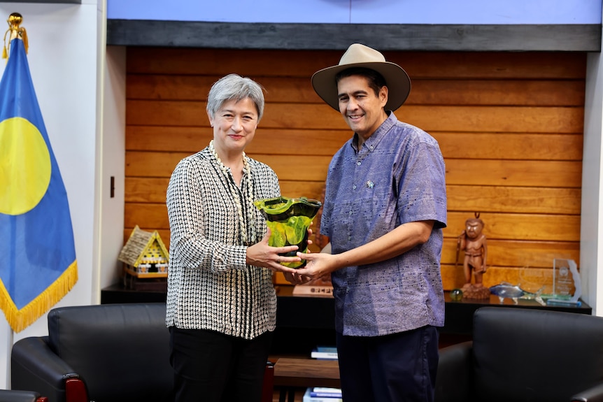 Penny Wong and Surangel Whipps Jr, wearing an Akubra, hold a green vase and smile for photographers 
