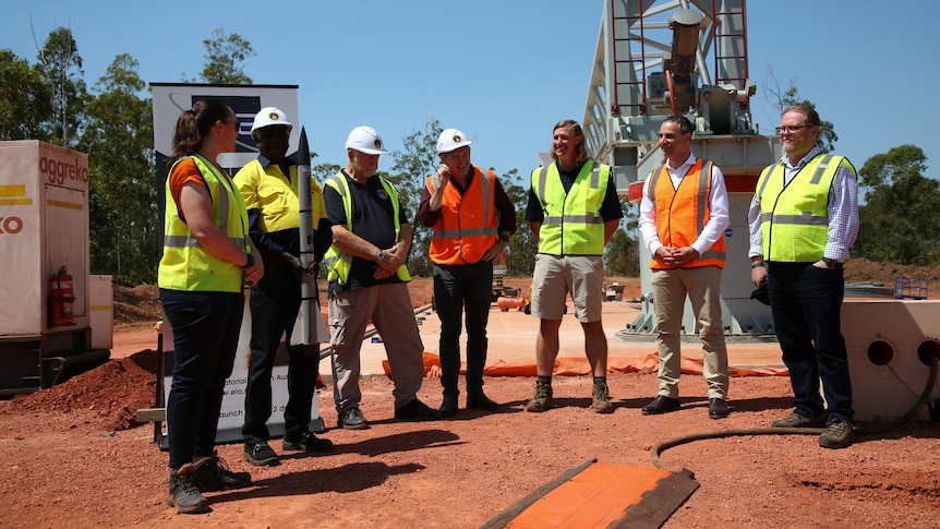 A group of people in high-vis vests stand around some space infrastructure.