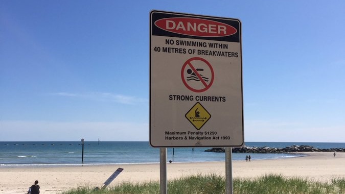 A warning sign in front of a beach with a breakwater