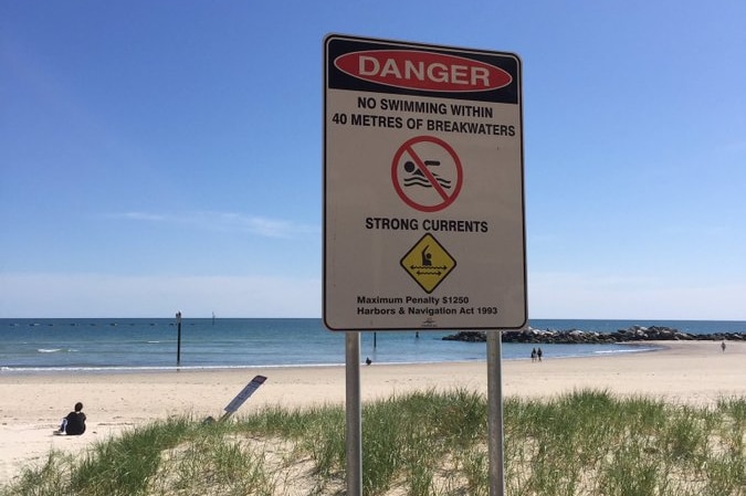 A warning sign in front of a beach with a breakwater