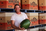 a man holding a watermelon in front of cardboard boxes