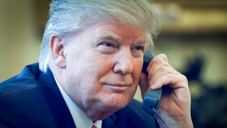 Donald Trump holds a phone to his ear with a slight grin on his face 