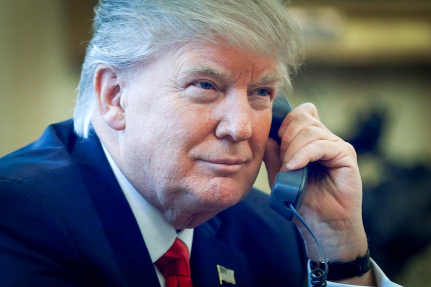 Donald Trump își ține un telefon la ureche cu un zâmbet ușor pe față 