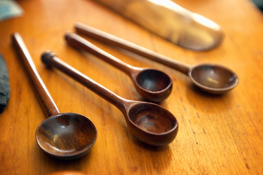 Some hand carved wooden spoons lying on a wooden surface.