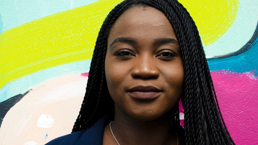 Prudence Melom standing in front of a coloured wall for a story about refugees in regional Australia sharing their stories