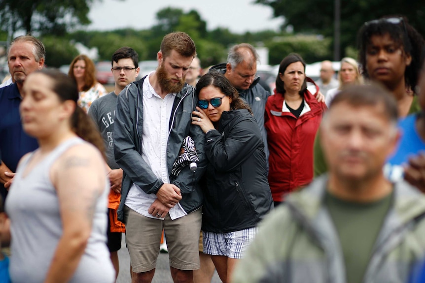 A man and a woman huddle together crying, the pair standing among a crowd of others