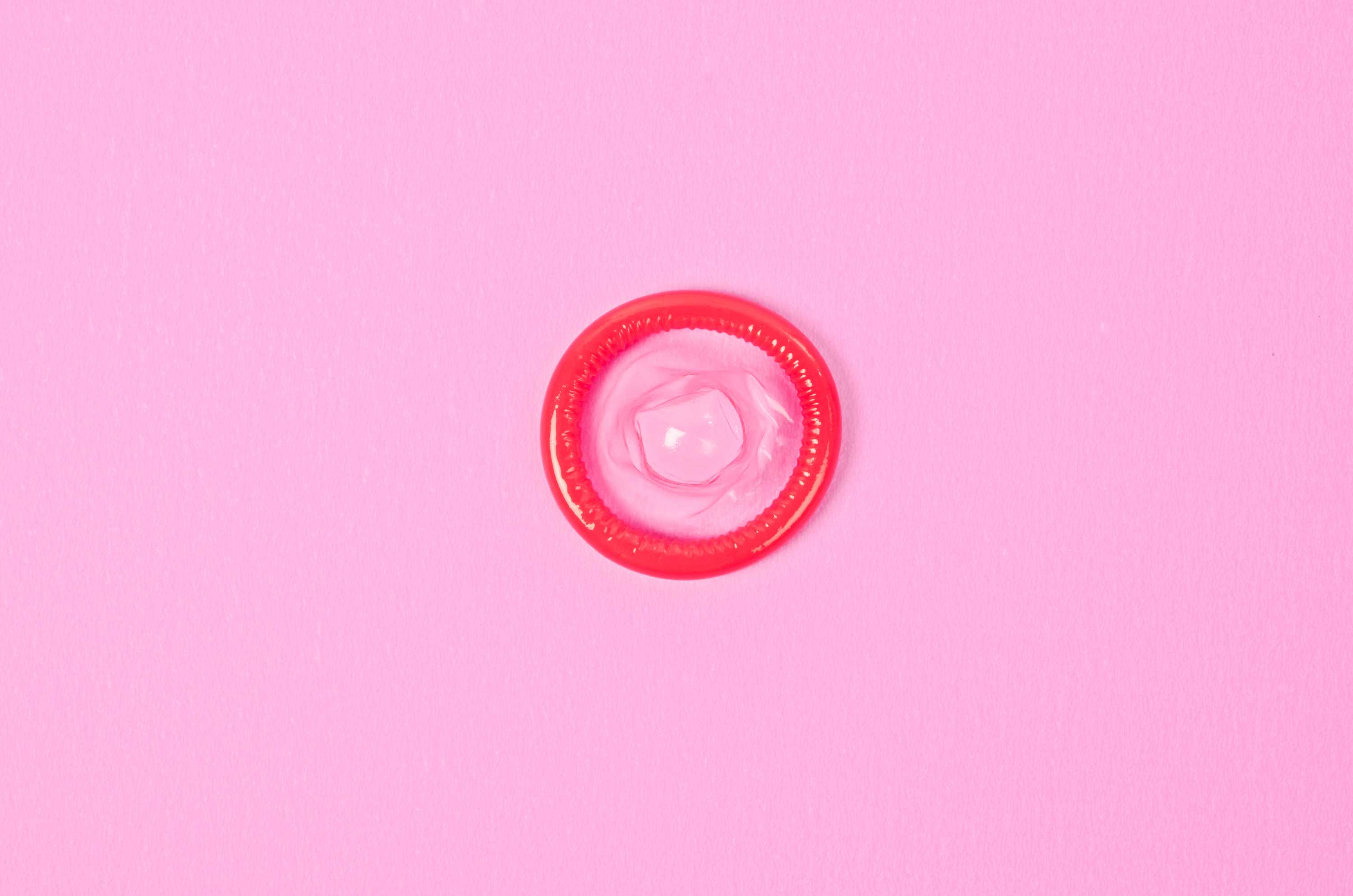 Pink condom rolled up on pink background.