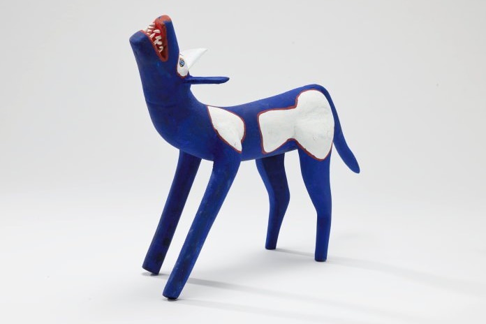 A wooden carving of a stylised dog painted blue and white arching its back and baring its teeth. 