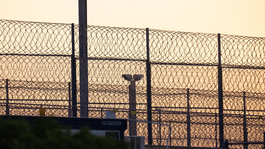 A barbed wire fence pictured against a sunset outside a prison