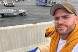 A man sitting in a wheelchair next to his service dog on an airport tarmac