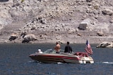 Two people on a small boat with an american flag on the back look up at the towering rocky walls that enclose the lake