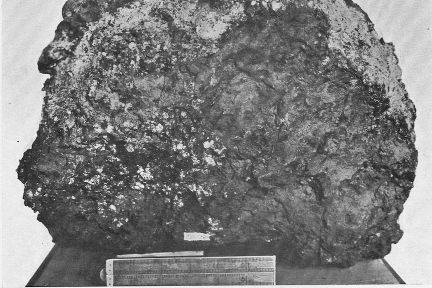 A black and white photograph of a large meteorite with a ruler below it