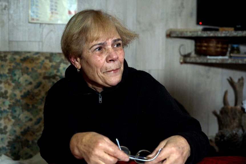A woman in wearing black holding her glasses, appearing to be on the brink of tears.