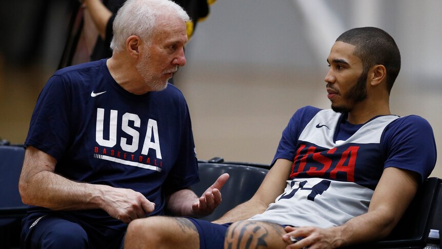 Gregg Popovich leans forward and motions with his hands as he sits next to Jayson Tatum, who is reclined next to him