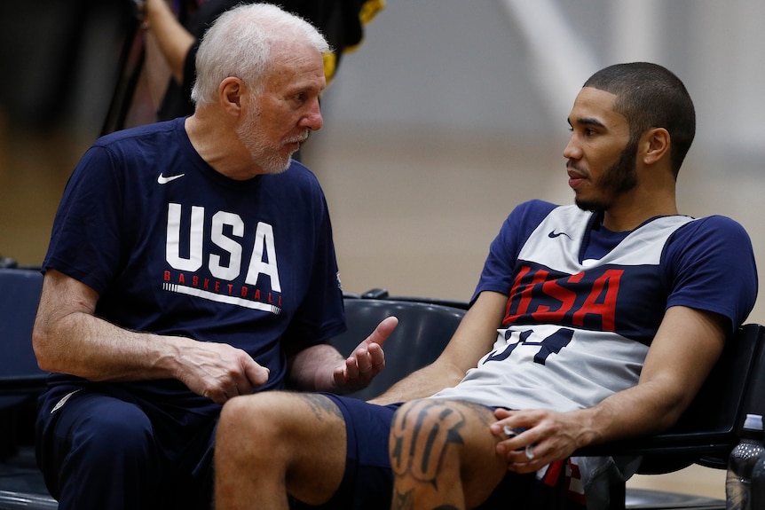Gregg Popovich leans forward and motions with his hands as he sits next to Jayson Tatum, who is reclined next to him
