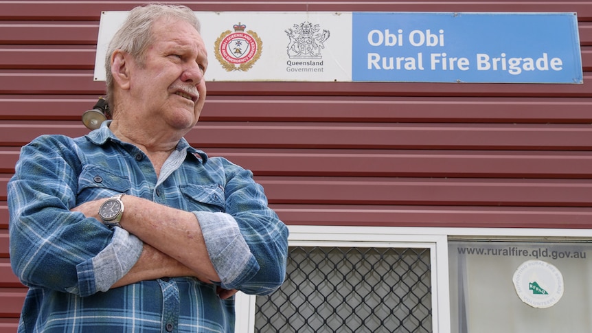 elderly man standing out the of fire station with arms folded 