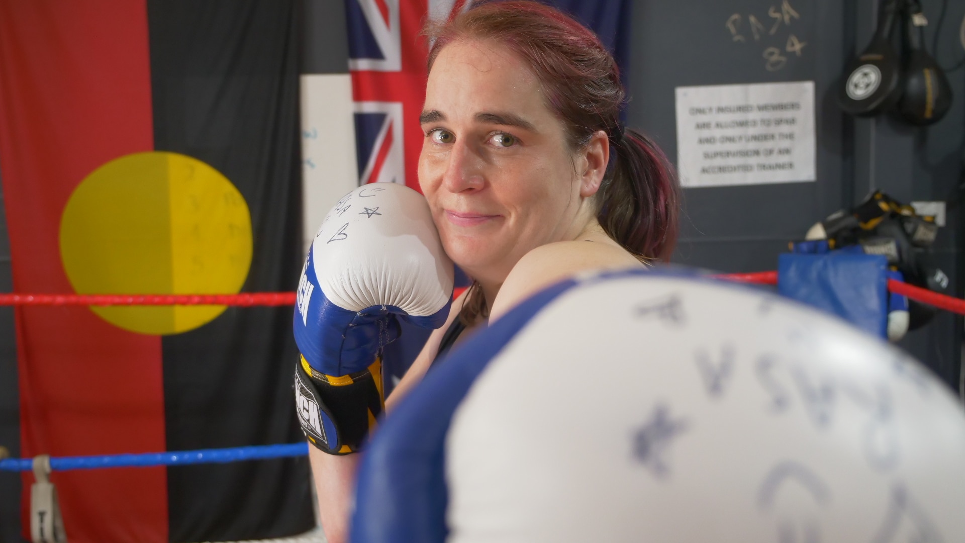 Luva de boxe para câmera e mulher sorrindo com a outra luva na bochecha.
