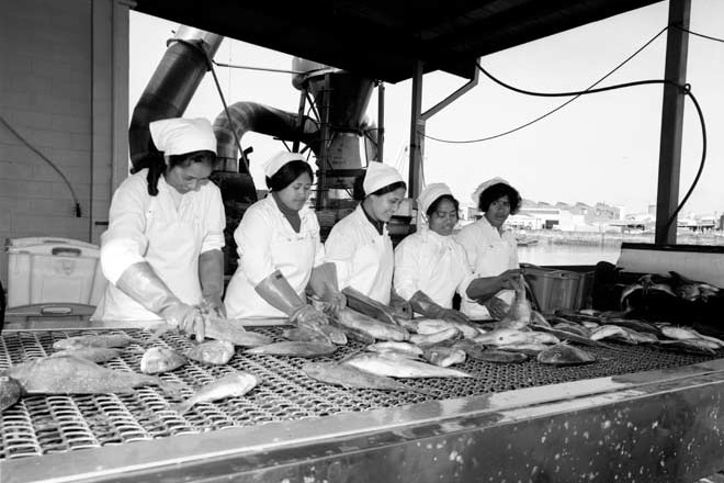 A black and white image shows five women working on a production line. 