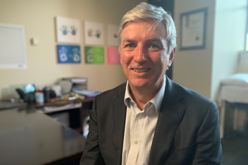 David McCombe smiling in an office, decorated with hand prints pictures.