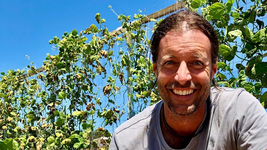 A farmer kneels in front of a vine with a freshly dug beetroot in his hands